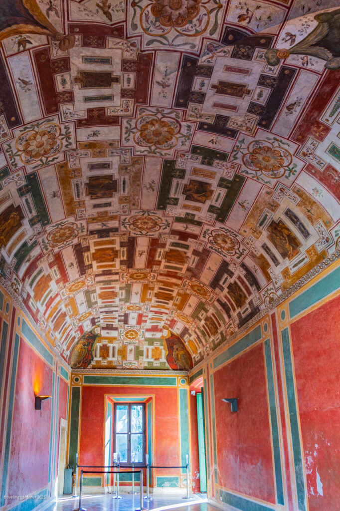 Vaulted ceiling covered in intricate geometric and floral frescoes in red, gold, and green inside a historic room.