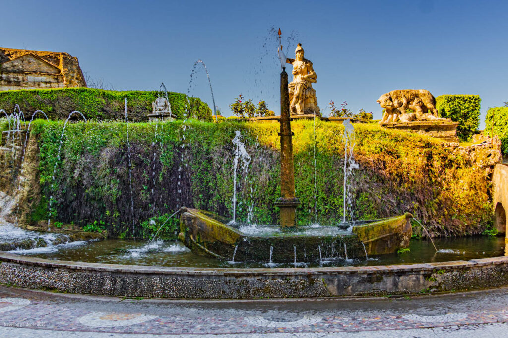 Fountain with a central obelisk and statue atop a terraced garden under a clear blue sky