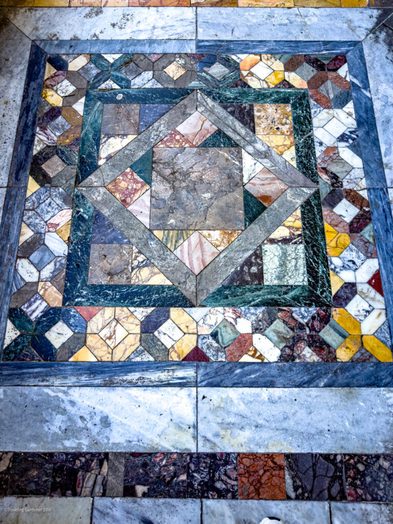 Intricate geometric marble mosaic on a floor with concentric squares in blue, green, and earth tones.