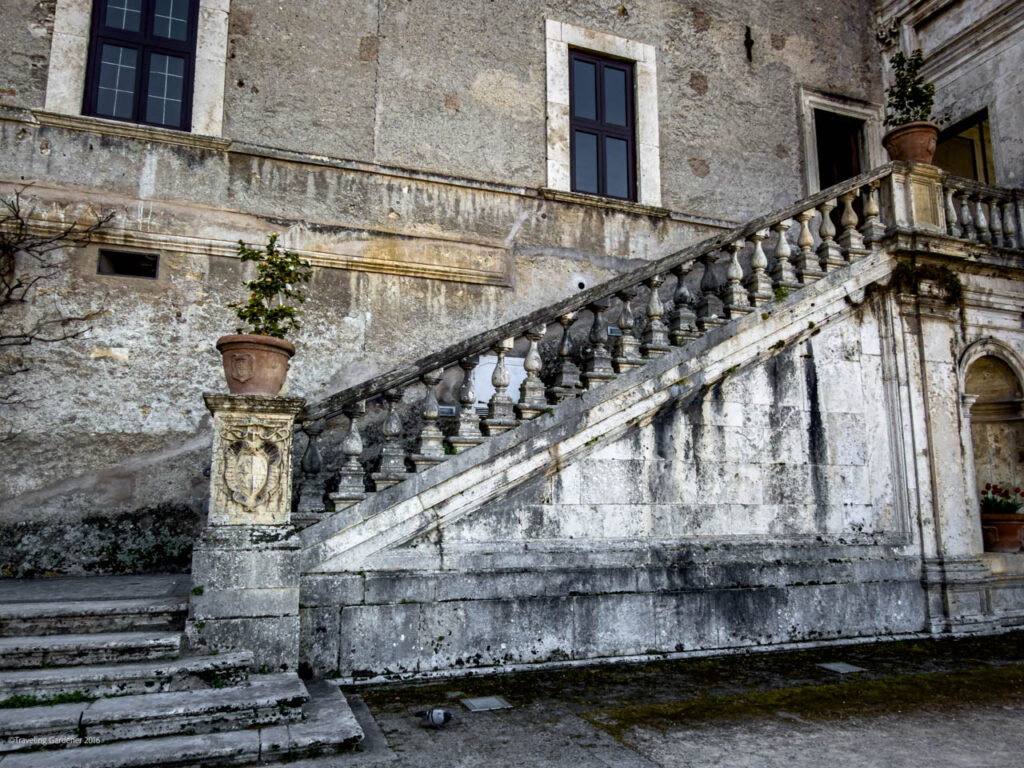 Old stone building with a grand, mossy staircase and carved balustrade, potted plants on pedestals at the top and bottom.