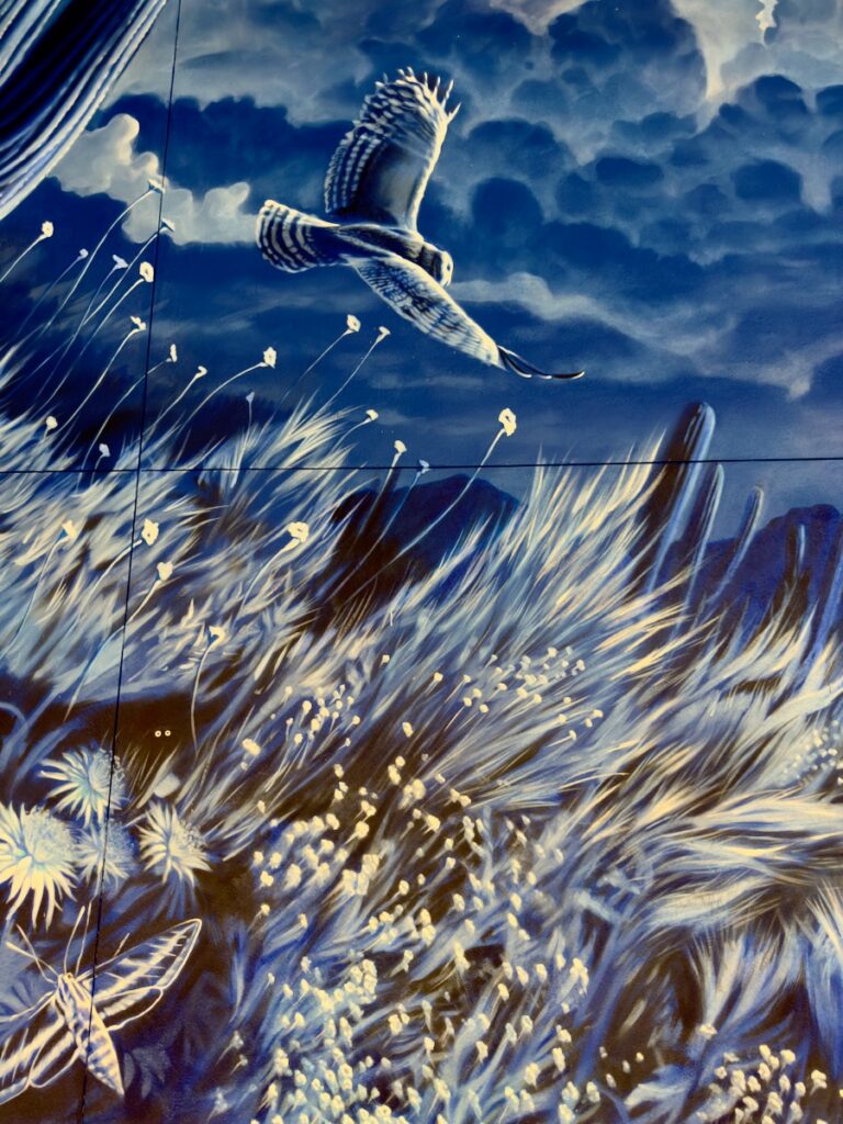Blue-toned mural of a seabird soaring over tall grasses and abstract flowers.