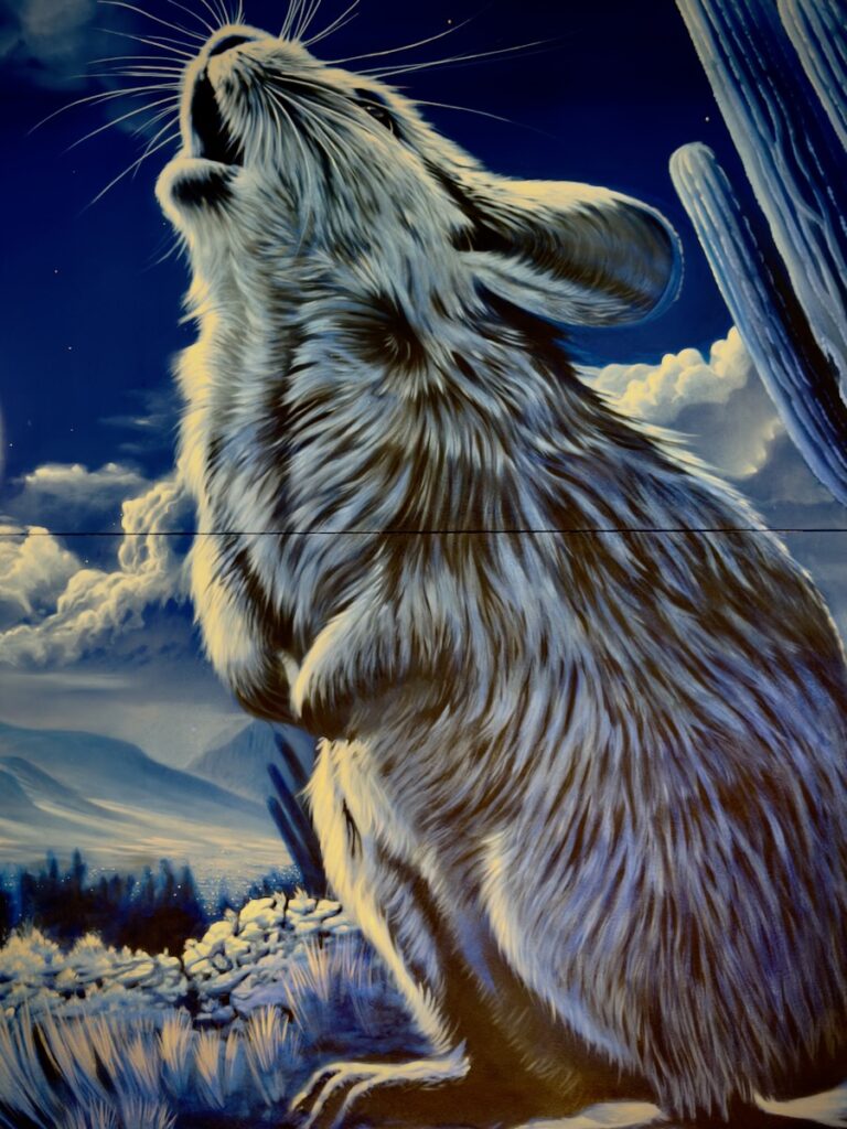 Blue-toned mural of a rabbit standing on snow with head raised toward the sky, fur rippling in icy blues and whites.