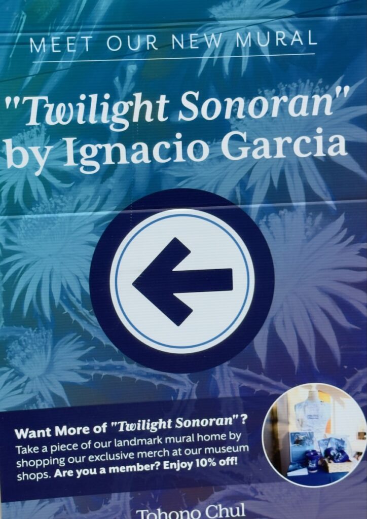 Poster for the mural "Twilight Sonoran" by Ignacio Garcia, with a large left arrow on a blue floral background.