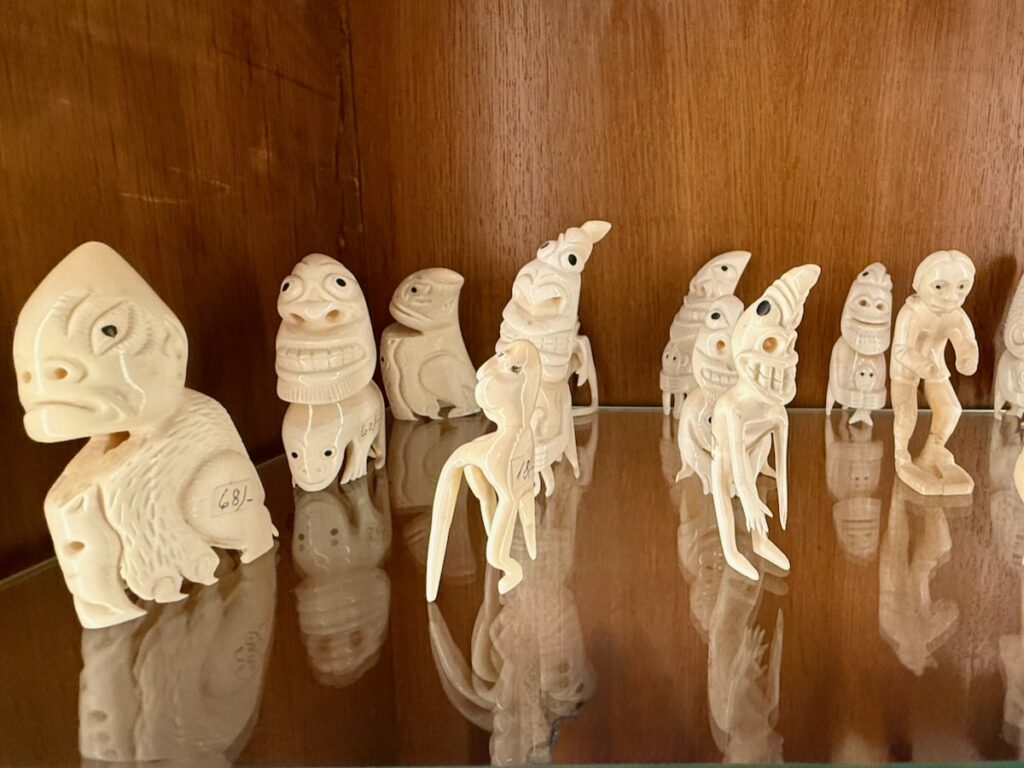 Collection of white carved dinosaur-like figurines on a glass shelf against a wooden wall.